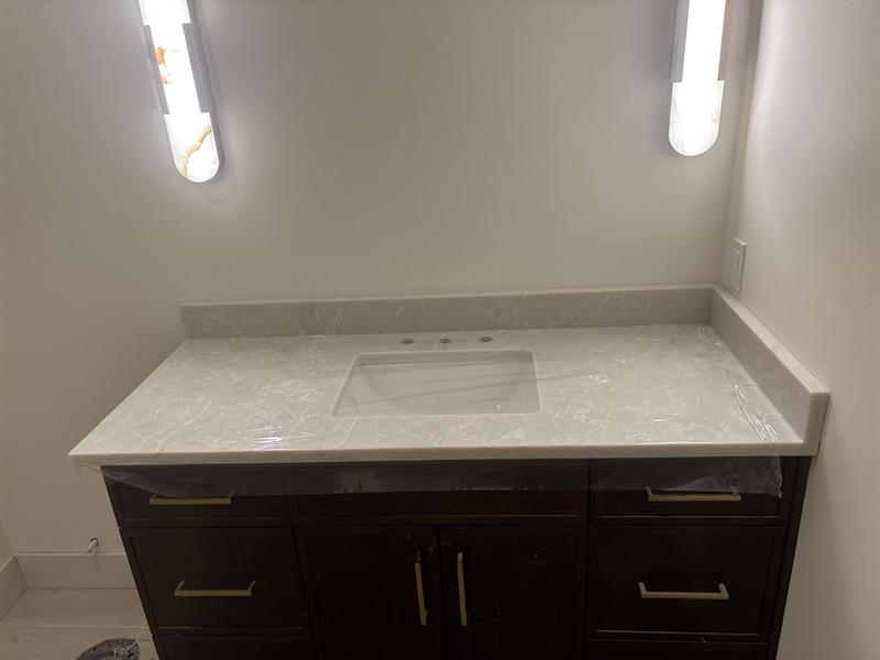 Espresso bathroom vanity with brass pulls and a light grey veined quartz top with backsplash