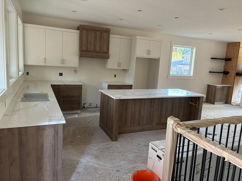 Two-tone kitchen with white flat-panel uppers, brass pulls, a walnut-tone hood and island, and white quartz counters